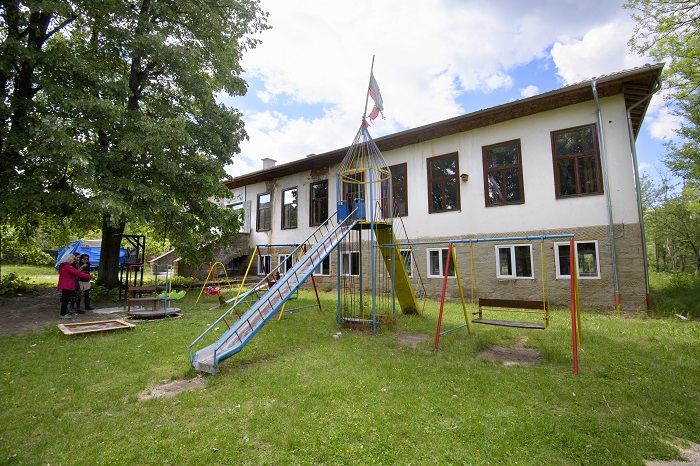 Обновената с помощта на хората от селото детска площадка; зад нея е почти завършената сграда на училището, в което се помещават школата по рисуване към читалището и детската градина, която предстои да отвори врати